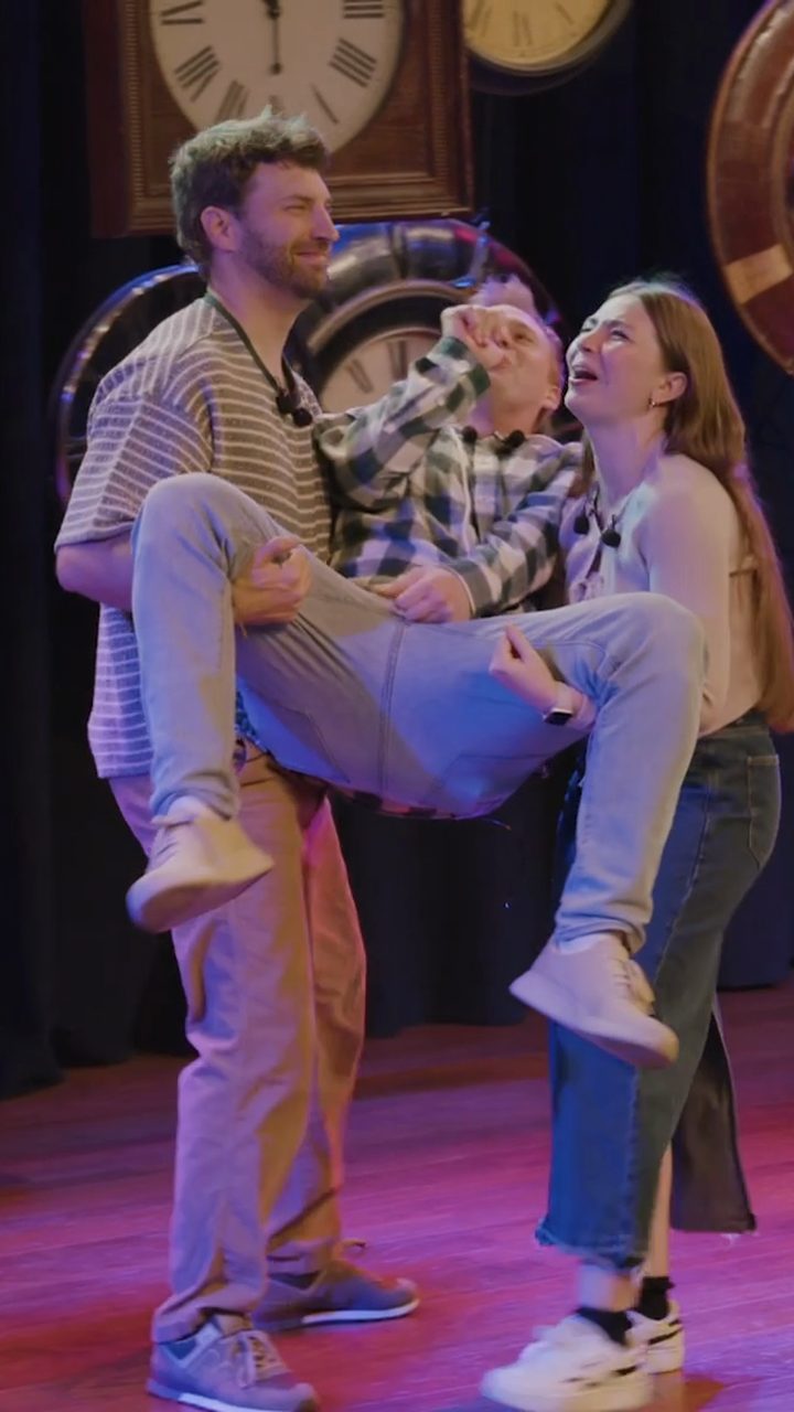 Zach carries a castmate across the stage while Shae laughs